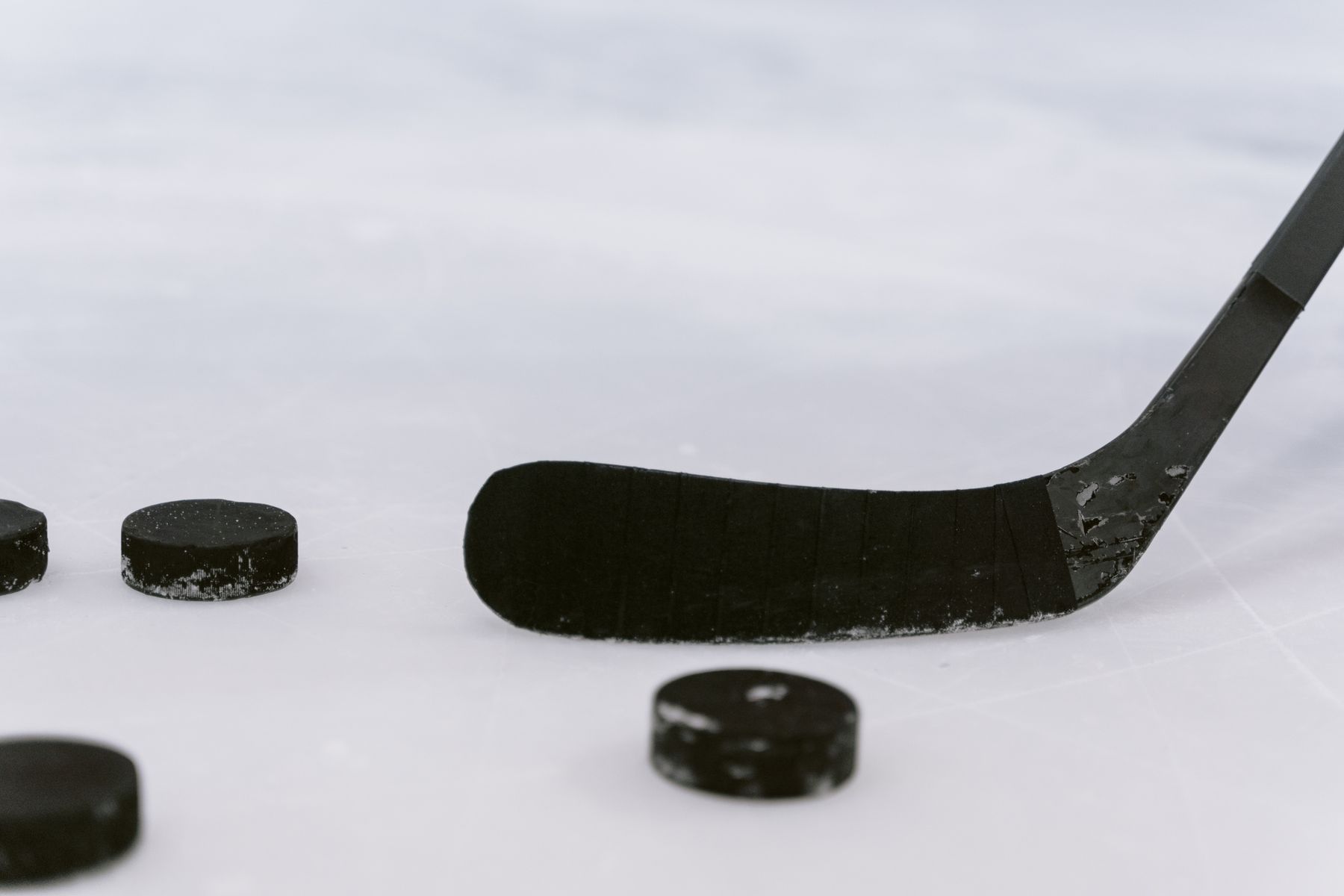 Close-up of a worn black hockey stick blade and pucks on ice.